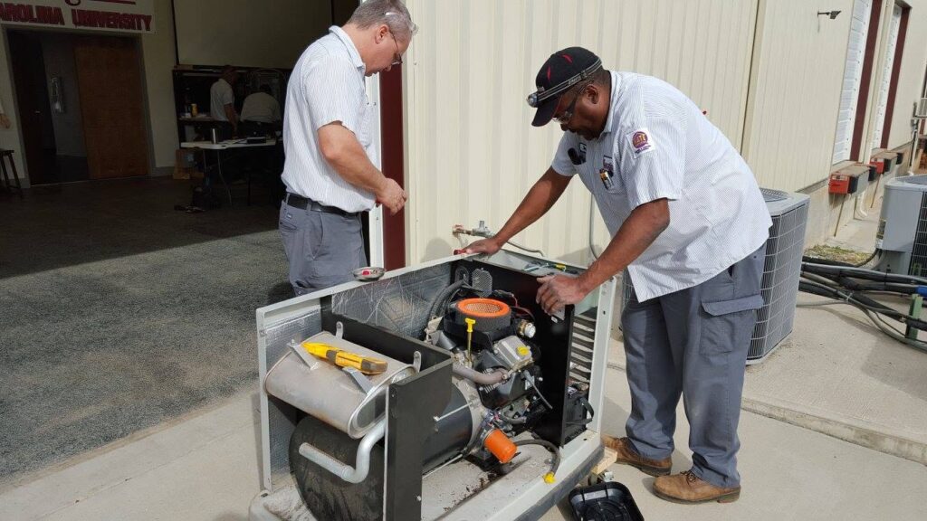 Two technicians service a portable generator outside a building, inspecting the engine with tools nearby