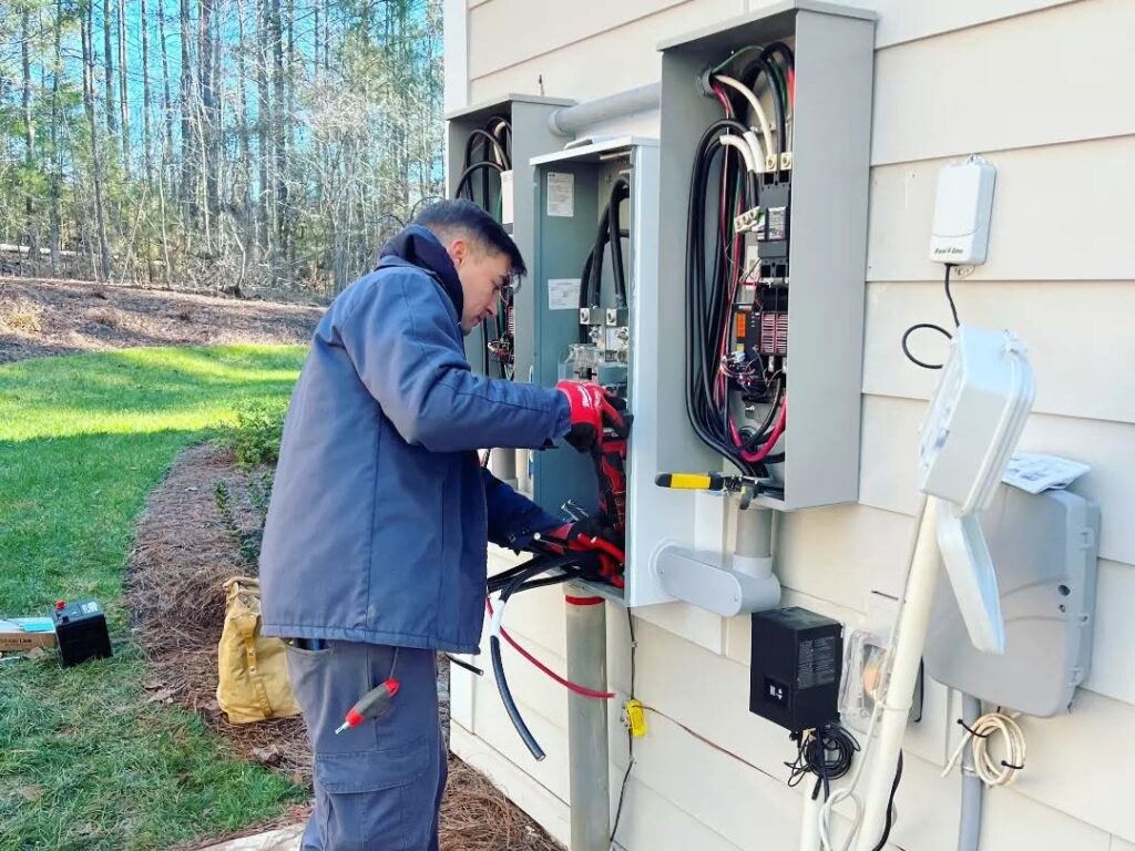 Technician in blue workwear repairing an outdoor electrical panel on a house.